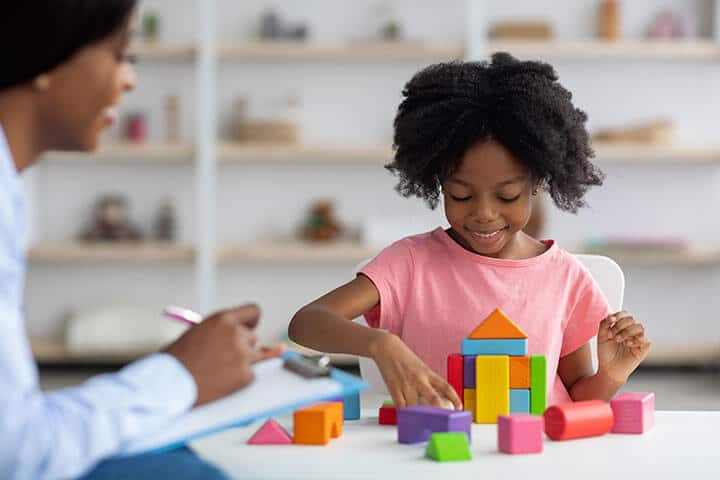 young girl playing with blocks while therapist observes